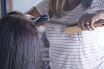 Hairstylist using curling iron of female client in hairdressing salon, closeup view. Hairdressing services. Creating hairstyle. Hair styling process.