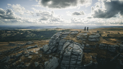 Fototapeta na wymiar A drone shot of two people standing on the rocky hill in Dartmoor country park