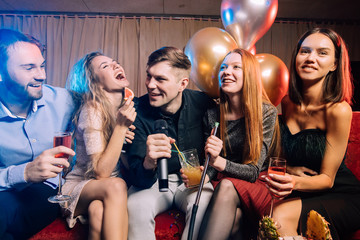 young women and men clubbers spend time in karaoke bar, have fun singing in microphone. leisure, celebration, party concept - obrazy, fototapety, plakaty