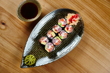Close up view sushi roll maki with tuna and salmon, cream-cheese, tobiko caviar on a black plate with soy sauce. Japanese food