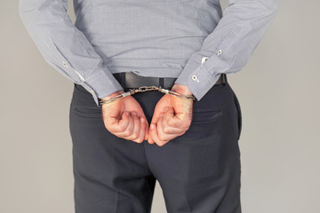 Arrested man handcuffed hands at the back. Isolated on gray background. Businessman in office in...