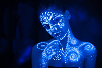 Body art on the body and hand of a girl glowing in the ultraviolet light.