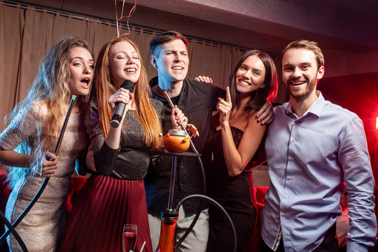 Group Of Young Caucasian People In Party Clothes Have Free Time. Leisure Time In Karaoke Bar, Enjoy Singing, Drinking