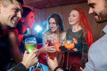 caucasian group of friends drink and have fun togeher in karaoke bar, beautiful girls and handsome guys chilling out and rocking together, have leisure time