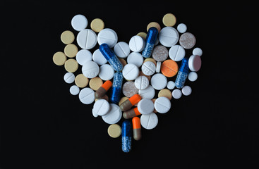 Heap of colorful pills in the shape of a heart, tablets and capsules over black background
