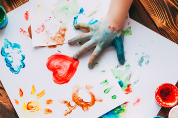 Close-up of child hand painting colorful mosaic. The child is drawing his palm on white sheets with...