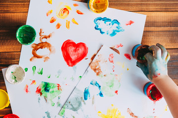The child putting his hand in a jar of paint and drawing colorful mosaic on white sheets with...