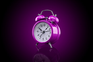 Purple alarm clock with reflection on glass close-up isolated on dark background with purple...