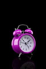 Purple alarm clock with reflection on glass close-up isolated on dark background.