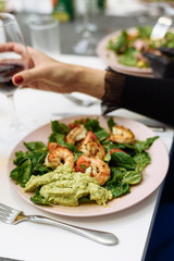 Fried prawns on a dish with spinach and guacamole pasta salad. The girl drinks red wine from a glass and eats an expensive dish in a restaurant