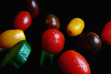 multicolored cherry tomatoes with sliced cucumbers in water drops on a dark background