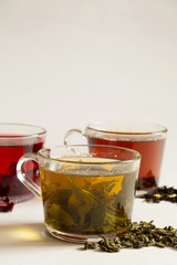 Green hot tea with dry leaves on a white. Three glass cups with black, red and green tea on a white background. Red hot Hibiscus tea. Black hot tea. Healthy lifestyle.Hot drinks. vertical orientation