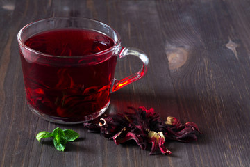 Healthy lifestyle. Glass cup of red hibiscus hot tea with dry flowers rose with fresh green leaves...
