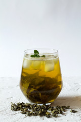 Green iced tea in a glass on white background. Healthy lifestyle. Glass of iced green herbal tea and dry leaves with fresh green leaves of mint on a white table. Cold drinks. vertical orientation.