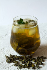 Glass of iced green herbal tea and dry leaves with fresh green leaves of mint on a white table. Green iced tea in a glass on white background. Healthy lifestyle. Cold drinks. vertical orientation.