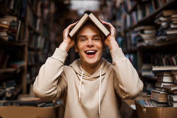 Happy student with book above his head, funny and joyful concept, smiley face of caucasian man...
