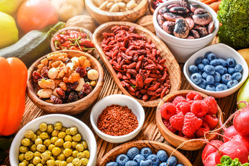 Healthy food eating variety selection in bowls: vegetables, fruits, berries, seeds, superfood, cereal, leaf vegetable on colorful background.