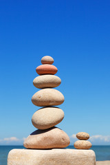 Fototapeta na wymiar High Rock zen pyramid of white and pink pebbles on a background of blue sky and sea.