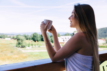 the girl closed her eyes and drinking hot coffee on the balcony