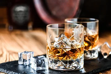 Fotobehang Glas whisky met ijsblokjes op zwarte stenen tafel. Zijaanzicht met kopie ruimte alcohol concept. © Milan