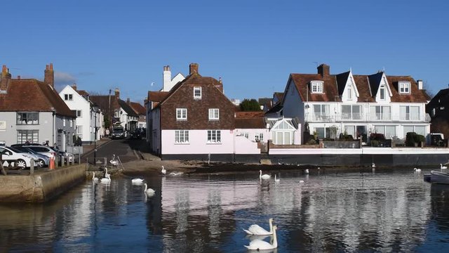 Emsworth harbour view where the road from the HIgh Street meets the waters edge which has swans and buildings reflecting in the water.