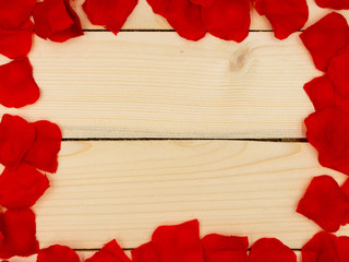 Red rose petals forming a frame on a wooden table.