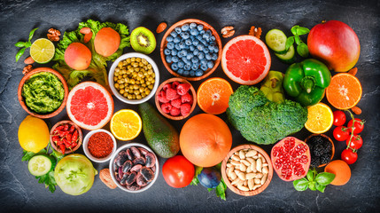 Healthy superfood eating variety collection in bowls: vegetables, citrus fruits, berries, seeds, raw food, cereal, leaf vegetable on colorful background.