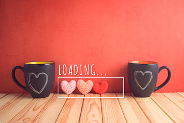 Valentines day concept with chalkboard coffee mugs, heart shapes and  loading love text on wooden table.