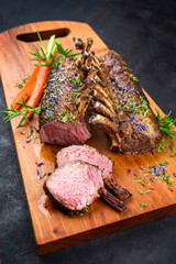 Barbecue rack of lamb with carrot and herbs offered as closeup on a modern design wooden board