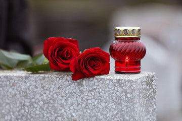 Red roses and candle on light grey tombstone outdoors. Funeral ceremony