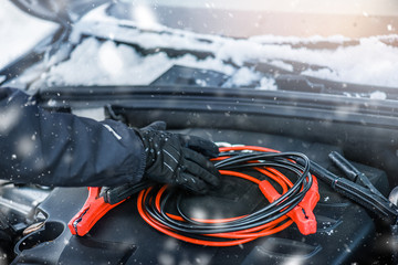 Hands charging car battery with electricity trough electric cables. Vehicle jumper cable cars...