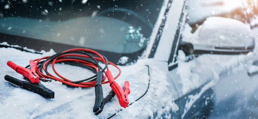 Charging cars battery with electricity trough electric cables. Vehicle jumper cable on car need starting or connection in winter time. Banner or panorama photo.