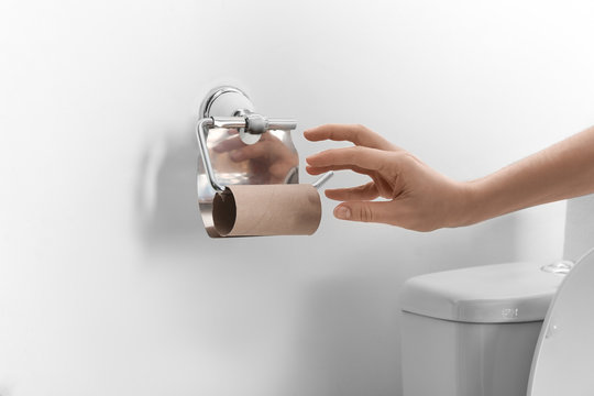 Woman Reaching For Empty Toilet Paper Roll In Bathroom, Closeup