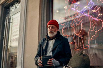 Hungry mature man with grey beard sit on street asking for help, money for shelter and food. Face...