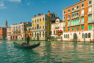Fototapeta na wymiar Venetian gondolier punting gondola through Grand Canal along colorful building facades in Venice