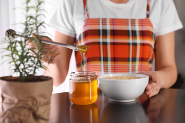 Woman adding honey to oatmeal at black table, closeup