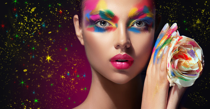 Beautiful girl with festive bright multi-colored make up  on the face. Young woman dressed in extravagant art makeup .Twinkling stars on a black background. Holiday ,celebration, cosmetic and beauty .