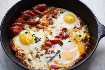 Hot homemade fried eggs with tomatoes and sausage in a pan closeup