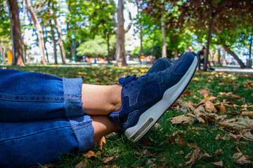 The leg of a young woman who lie down on the grasses with blue jeans and blue shoes