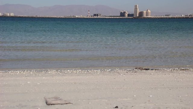 white sand beach and calm sea in sunny day with background of Ras Al Khaima city in Emirates