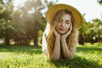 curly blonde looks sadly at the camera while lying on the park grass and props her cheeks with her palms