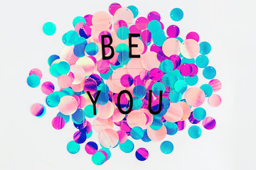 Background with shiny pink, purple and holographic sequins with words Be you, abstract background.