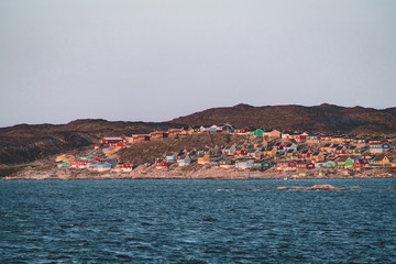 Fototapeta na wymiar Aerial View of Arctic city of Ilulissat, Greenland during sunrise sunset. Colorful houses in the center of the town with icebergs in the background in summer on a sunny day with orange pink sky