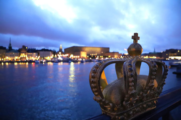 Gilded Crown on Skeppsholmsbron by dusk with dramatic dark collored sky at the river with a view at Gamla Stan in Stockholm Sweden. Focus is on the Crown.