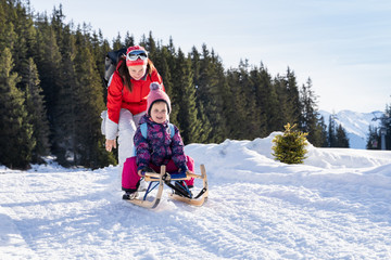 Fototapeta na wymiar Girl Enjoying Sledding With Her Mother Against Winter Forest