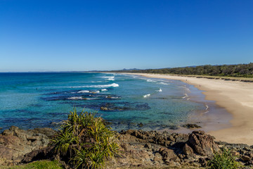 Small waves on a surf beach with sandy beach and green tropics behind ocean