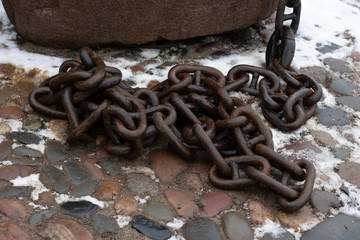 Old chain on the background of the pier. Rusty anchor chain piled up on the pier, close-up
