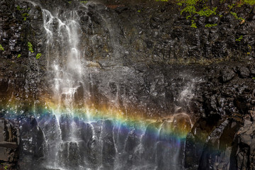 Small rainbow created by flowing water over black jagged rocks