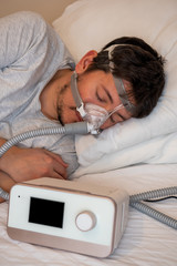 Healthy young man wearing ( CPAP Mask ) nasal mask and using CPAP machine for sleeping smoothly all night long on his left side cross arms without snoring. sleep apnea therapy. selective focus.