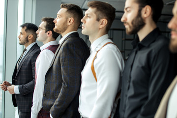 Fototapeta na wymiar side view on young caucasian bearded business people, successful men looking side at window, everyone in stylish elegant tuxedo. isolated in modern office